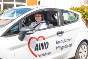 Eine Pflegekraft sitzt in einem Auto des Pflegedienstes. - AWO Forchheim