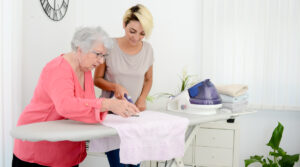 Eine junge Frau hilft einer älteren Frau beim Bügeln. - AWO Forchheim