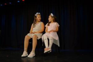 Zwei Mädchen sitzen verkleidet auf einer Bühne und unterhalten sich.