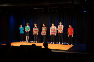 Sieben Grundschüler*innen stehen auf einer Bühne