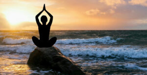 Eine Person sitzt auf einem Felsen am Meer und meditiert